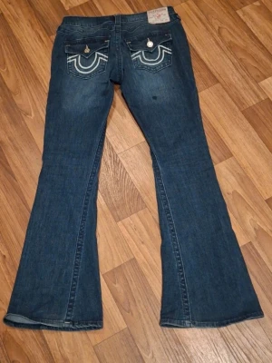 Helt nya blå bootcut jeans från True Religion.Endast använda ett par ggr. - Säljer ett par blå bootcut jeans från True Religion med ikoniska kontrastsömmar och snygga fickdetaljer bak. Jeansen har låg midja och klassisk femficksdesign. Tillverkade i slitstarkt denim med lätt tvättad look.