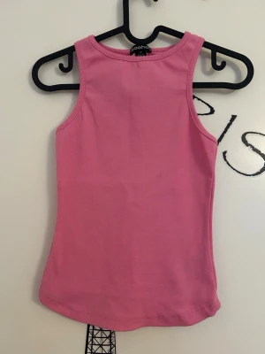 Rosa ribbad linnetopp från Boohoo - Rosa ribbad linnetopp från Boohoo i storlek XS. Toppen är ärmlös med rund halsringning och är i längre rundad modell framtill. Toppen är i nytt skick då den aldrig är använd. 