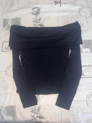 Svart offshoulder topp - Trendig svart offshoulder topp med långa ärmar. Snygg och enkel design som passar perfekt till många olika outfits. Mjuk och stretchig känsla, perfekt för dig som gillar stilrena plagg.