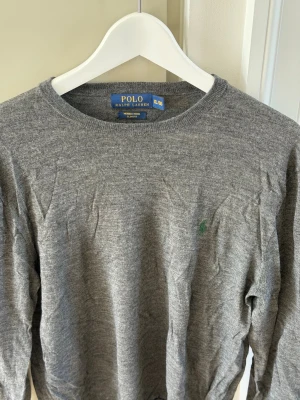 Polo Ralph Lauren Merino Wool Slim Fit  - Snygg grå stickad tröja från Polo Ralph Lauren i merinoull. Slim fit-modell med rund halsringning och diskret grön logga broderad på bröstet. Knappt använd, mycket gott skick. Hör av er vid frågor! Nypris ca 2400