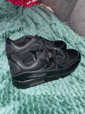 Helsvarta Nike Air Max sneakers - Säljer ett par helsvarta Nike Air Max sneakers med klassisk chunky sula och snygga detaljer i läder och mesh. Skorna har svarta skosnören och diskret Nike-logga på sidan. Perfekta för dig som gillar en clean och sportig look.