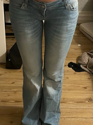 Ljusblå bootcut jeans - Säljer ett par ljusblå bootcut jeans med låg midja och klassisk femficksmodell. Jeansen har en snygg tvätt med slitningar framtill och är tillverkade i ett mjukt denimtyg med lite stretch. Perfekta för en avslappnad och trendig look.