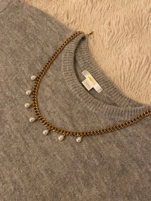 Guldfärgat halsband med pärlor - Snyggt halsband i guldfärgad metall med kedja och hängande vita pärlor. Perfekt för att ge din outfit en elegant touch. Klassisk design som passar till många olika stilar.