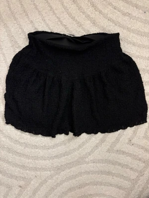 Svarta högmidjade shorts i bouclé - Säljer ett par svarta högmidjade shorts med lös passform och vågig kant. Materialet är bouclé-liknande och ger en cool textur. Perfekta för sommarens alla tillfällen och riktigt sköna att bära.