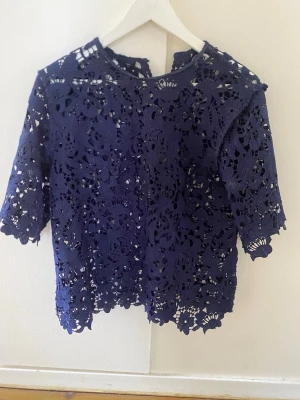 Zara blus  - Säljer en mörkblå blus i genombruten spets med blommönster. Blusen har halvlånga ärmar och rund halsringning. Materialet är tunt och luftigt, perfekt för lager på lager. Supersnygg till både jeans och kjol!
