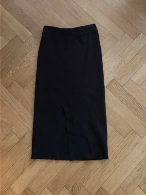 Svart långkjol med slits - En stilren svart långkjol med slits framtill. Kjolen har en rak passform och är enkel att matcha med olika toppar. Perfekt för dig som gillar minimalistisk stil.