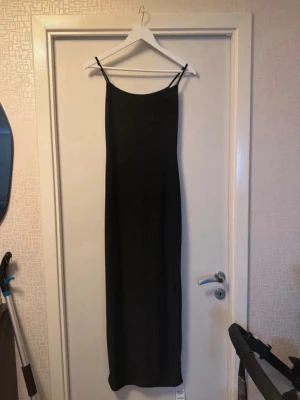 Svart långklänning från Boohoo - Säljer en svart långklänning från Boohoo med smala axelband och rak passform. Klänningen har en minimalistisk design och är perfekt för dig som gillar enkel stil. Materialet känns mjukt och följsamt, troligen polyester.