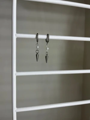 Silvriga örhängen med konformad hängare - Säljer ett par coola silvriga örhängen med små konformade hängen. Örhängena har en minimalistisk design och är tillverkade i metall med en blank finish. Perfekta för dig som gillar en edgy och stilren look. Handgjort 