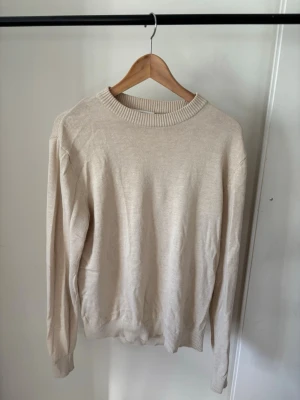 Beige stickad tröja - En stilren beige stickad tröja med rund halsringning och ribbade muddar vid ärmslut och nederkant. Tröjan har en enkel och klassisk design som passar till det mesta. Materialet ser mjukt och tunt ut, perfekt för lager på lager.