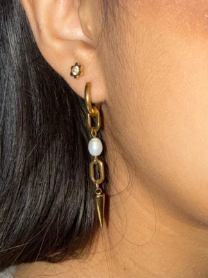 Guldiga örhängen med sötvattenpärla och spikdetalj - Priset avser ett par örhängen. Matchande halsband finns i en separat annons. Finns även i silverfärg.  Material: Guldpläterat rostfritt stål och sötvattenpärla Längd: ca 5,0cm Nickelfria och handgjorda