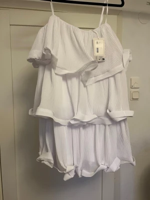 Vit omlottklänning med volanger - Säljer en superfin vit omlottklänning med tunna axelband och flera lager volanger. Klänningen har en luftig och flowy passform, perfekt för varma dagar. Materialet är lätt och känns skönt mot huden. Perfekt för dig som vill ha en söt och trendig sommarklänning eller studentklänning!