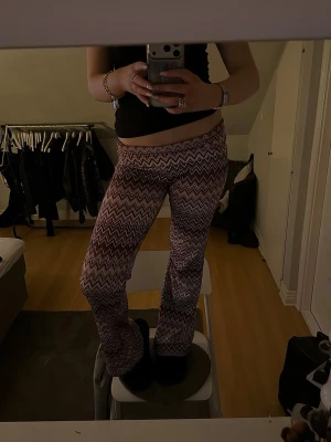 Mönstrade bootcut leggings - Säljer ett par snygga leggings med bootcut-modell och zigzag-mönster i vinrött, vitt och rosa. De har låg midja och stretchigt material som sitter skönt på kroppen. Perfekta för dig som vill ha något trendigt och bekvämt. passar nog väldigt många storlekar. 
