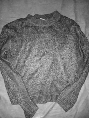 Svart stickad tröja från KappAhl - Snygg svart stickad tröja från KappAhl i storlek XS. Tröjan har ett diskret hålmönster, ribbade muddar vid ärmslut och nederkant samt en högre rund hals. Perfekt för lager på lager och enkel att matcha med olika outfits.