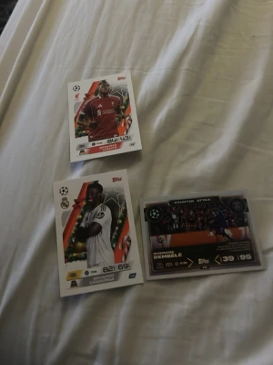 Samling fotbollskort Topps - Tre fotbollskort från Topps med färgstarka motiv och spelare i olika matchställ. Kort i vitt, rött och svart med detaljer i guld och orange. Ett av korten har texten 'Counter Attack' och visar en spelscen. Perfekt för samlare av sportkort.