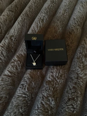 Silverhalsband från Maria Nilsdotter - Snyggt silverhalsband från Maria Nilsdotter med ett hängsmycke i form av en liten stjärna. Kedjan är tunn och halsbandet är inte använt en ändå gång eftersom att jag själv föredrar guld smycken. Säljer den för 900 vilket är en ganska bra pris man kan ändå tänka mig att förhandla. Halsbandet kommer i original box och påse.