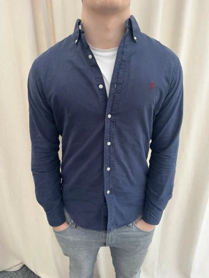 Marinblå skjorta från Ralph Lauren - Riktigt snygg skjorta från Ralph Lauren. Strl M, personen på bilden är 184 cm lång. Skicka gärna prisförslag. Kika in min profil för mer schyssta plagg.