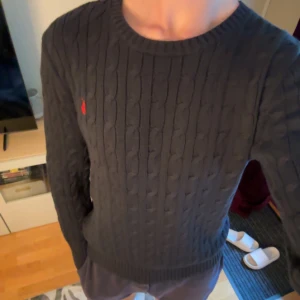 Kabelstickad Ralph Lauren Tröja - Mörkblå (Stl M) - Snygg mörkblå kabelstickad tröja från Ralph Lauren. Tröjan är i gott skick och är i barnstorlek XL vilket motsvarar herrstorlek M. Passar perfekt för höst och vinterdagar med ett nypris på ca 2200kr