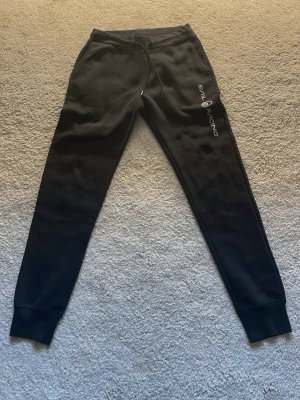Svarta mjukisbyxor från Sail Racing - Säljer ett par svarta mjukisbyxor från Sail Racing med logga på vänster lår. Muddar vid bensluten och en bakficka. Perfekta för chill dagar eller träning. Hör av er vid minsta fundering mvh Artur