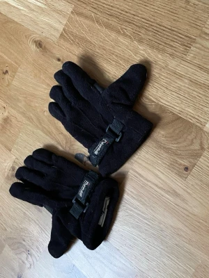 Svarta fleecehandskar från Tenson - Mysiga svarta fleecehandskar från Tenson med justerbart spänne vid handleden. Perfekta för kalla dagar och har en enkel, stilren design som passar till det mesta.