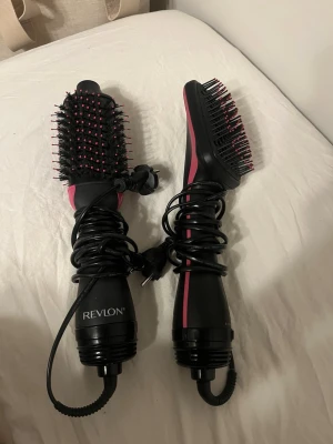 Revlon varmluftsborstar svart/rosa - Två elektriska varmluftsborstar från Revlon i svart med rosa detaljer. Ena är en värmeborste obs båda är varmLUFTsborstar . Perfekt för att styla och torka håret samtidigt.  Perfekt om du vill styla ditt hår men inte skada det. Ena är inte använd och den är använd 5 gånger. Runda borsten för 300 den andra för 200 båda för 450