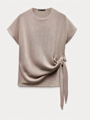 Beige topp med knyt i sidan Zara - Stilren beige topp från Zara med rund halsringning och korta ärmar. Toppen har en snygg knytdetalj i sidan som ger en unik twist till looken. Perfekt att matcha med både jeans och kjol för en trendig outfit.