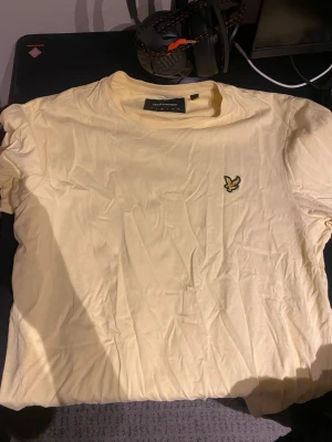Gul t-shirt från Lyle & Scott - Snygg gul t-shirt från Lyle & Scott med klassisk rund hals och ikonisk logga broderad på bröstet. Tillverkad i mjuk bomull och har en normal passform. Perfekt för en avslappnad och stilren look.