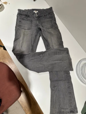 Grå bootcut jeans med stora fickor - Säljer ett par grå jeans bootcut  och stora framfickor. Jeansen har även klassiska bakfickor och knappgylf. Materialet är denim och färgen är tvättad grå, vilket ger en avslappnad look.