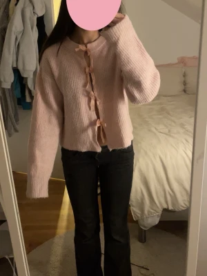 Ljusrosa kofta med rosetter Gina Tricot - Supersöt ljusrosa kofta från Gina Tricot i stickat material. Koftan har långa ärmar och stängs framtill med flera små rosetter, vilket ger en gullig och trendig look. Perfekt att slänga på sig under kyligare dagar.