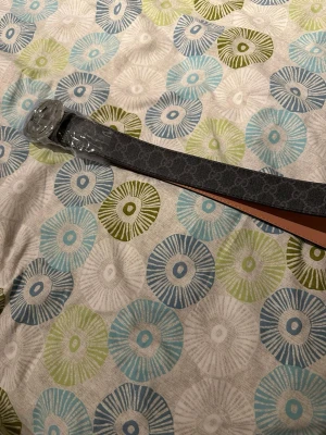 Svart bälte med GG-spänne - Snyggt svart bälte med det klassiska GG-mönstret längs hela bandet och ett stort silverfärgat GG-spänne. Bältet har en lyxig känsla och passar perfekt till jeans eller byxor för att lyfta din outfit.