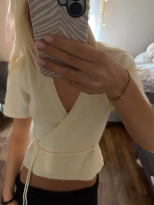 Vit omlottopp med knyt - Snygg vit omlottopp med korta ärmar och knyt i midjan. Toppen har en v-ringad design och är lätt croppad för en trendig look. Perfekt att styla med både jeans och kjol.