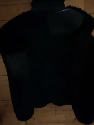 Svart teddyjacka från Axel Arigato - Säljer en svart teddyjacka från Axel Arigato med mjukt, fluffigt material och hög krage. Jackan har en stilren look och är helsvart med slät insida. Perfekt för dig som vill ha en trendig och bekväm jacka till hösten eller vintern.