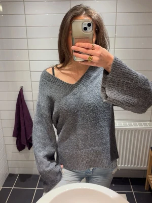 Grå oversized stickad tröja - Mysig grå stickad tröja med v-ringning och breda ärmar. Tröjan har en avslappnad, oversized passform och ribbstickade muddar vid ärmslut och nederkant. Perfekt för lager på lager och chill dagar.