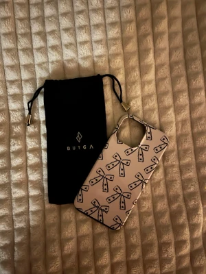 Burga mobilskal med rosett-mönster 13 PRO Max  - Snyggt mobilskal från Burga i hårdplast med vit bas och svarta rosetter över hela skalet.Skalet är knappt användt. Kommer med en svart tygpåse med Burga-logga.