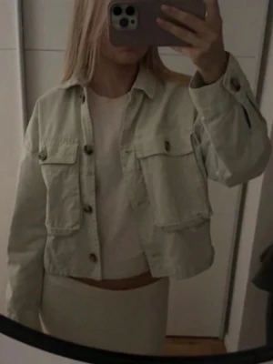 Ljus grön jeansjacka  - Trendig ljus jeansjacka i croppad modell med stora bröstfickor och knappar framtill. Klassisk krage och knappdetaljer vid ärmslut. Perfekt att slänga över en t-shirt för en avslappnad look.
