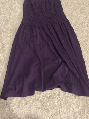 Lila axelbandslös klänning Wear It - Säljer en lila axelbandslös klänning från Wear It i storlek XS. Klänningen har smock upptill för en bekväm passform och ett mjukt, flowy tyg. Perfekt för varma dagar och enkel att styla med accessoarer.