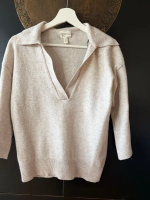 Beige stickad tröja med krage - Stickad tröja i mjuk beige nyans från H&M. Tröjan har en djup v-ringning, bred krage och trekvartsärmar. Ribbstickade muddar vid ärmslut och nederkant ger en snygg finish. Perfekt för dig som gillar en avslappnad men ändå stilren look.