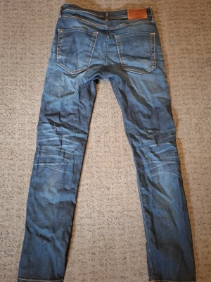 Blå jack & jones jeans - Säljer ett par blåa Jack & Jones med passform slim straight och klassisk femficksdesign, Storlek 29W 32L. Jeansen har snygga slitningar och kontrastsömmar. Perfekta för dig som gillar en tidlös och enkel stil. Skrive vid frågor.
