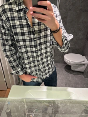 Rutig flanellskjorta svart vit  - Säljer en svartvit rutig skjorta med klassisk krage och knäppning framtill. Riktigt snygg nu till våren. Skjortan är i riktigt bra skick och har inga tecken på användning. Jag på bilden är 188cm och bär storlek M. Hör av er vid fler frågor eller prisförslag:)
