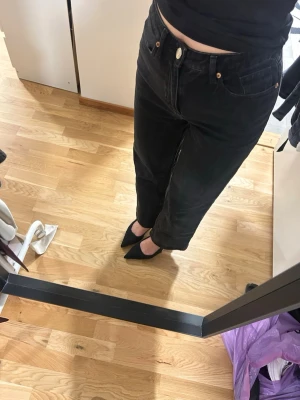 Svarta raka jeans med hög midja - Säljer ett par svarta jeans med rak passform och hög midja. Jeansen har klassiska fem fickor och stängs med knapp och dragkedja. Perfekta till sneakers eller klackar för en cool look.