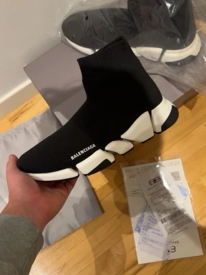 Balenciaga Speed Trainer 2.0 - Säljer ett par svarta Balenciaga Speed Trainer sneakers med vit chunky sula och stickad strumpliknande ovandel. Ikonisk logga på sidan och futuristisk design. Skorna är lätta och flexibla, perfekta för dig som gillar streetwear och vill sticka ut.