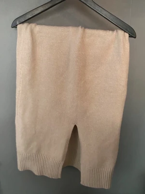 Beige stickad kjol med slits - Mysig beige stickad kjol med ribbad kant och en liten slits. Kjolen har en rak passform och är perfekt för dig som gillar en enkel men trendig look. Passar till både sneakers och boots.