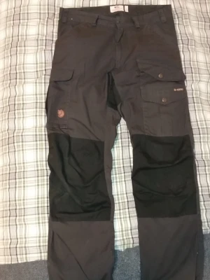 Fjällräven svarta cargobyxor - Köpta för 1500:- säljer för 850 kan eventuellt få ner. Snygga svarta cargobyxor från Fjällräven, Storlek EU: 48, US:32 med flera praktiska fickor och förstärkta partier över knäna. Byxorna har klassisk cargomodell med knappstängning och logga på benet. Perfekta för dig som gillar outdoor och streetstyle.