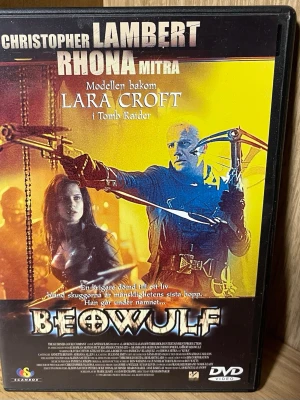 Beowulf DVD-film - Säljer en DVD-film med titeln Beowulf, med Christopher Lambert och Rhona Mitra i huvudrollerna. Omslaget har en mix av gult och svart med actionmotiv och fantasytema. Filmen är inspirerad av den klassiska berättelsen om Beowulf och är på svenska.