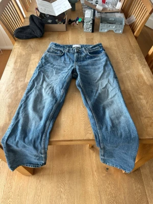 Blåa raka jeans i klassisk modell - Säljer ett par blåa jeans med rak passform och klassisk femficksdesign. Jeansen har en snygg tvättad look och är tillverkade i denim. Perfekta för en avslappnad stil och passar till det mesta.