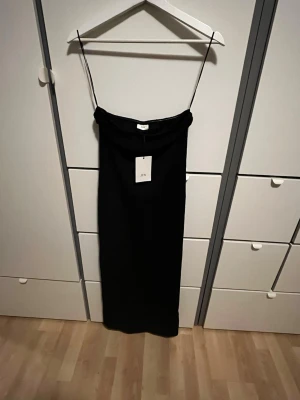 Svart tub-långklänning från JDY - Stilren svart långklänning från JDY utan band och rak passform. Klänningen har minimalistisk design och är perfekt för dig som gillar en enkel men elegant look. Tillverkad i mjukt material som känns skönt mot huden.