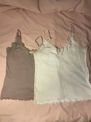 Två ribbade linnetoppar med spets storlek S-M - Säljer två ribbade linnetoppar med tunna axelband och spetsdetaljer vid urringningen. Ena toppen är beige och den andra är ljusvit, båda i mjukt material som sitter snyggt på kroppen. Perfekta att styla lager på lager eller till jeans. Har viss tecken på användning, som noppror. Det står att den beigea är storlek M och den vita är storlek XL- men dem båda sitter som S/M! 
