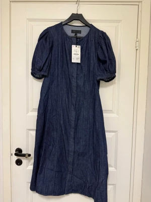 Blå jeansklänning från Zara med puffärm - Snygg blå jeansklänning från Zara med rund halsringning och puffärmar. Klänningen har en rak passform och är tillverkad i jeansmaterial, vilket ger en cool och avslappnad look. Perfekt för dig som gillar stilrena och trendiga plagg.Nypris 699kr