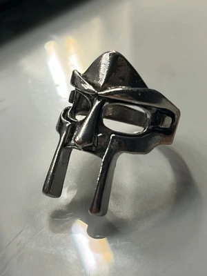 Silvrig ring med maskdesign - Cool ring i silverfärgad metall med en unik design som liknar en mask eller hjälm. Ringen har öppna detaljer för ögon och näsa, och är justerbar baktill för att passa olika fingrar. Perfekt accessoar för dig som gillar statement-smycken och streetstyle. Laila ring, använd ett fåtal gånger, justerbar orginal pris: 249kr mitt pris: 150kr