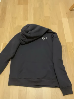 Mörkblå hoodie med rosa stjärna Ryuls - Cool mörkblå hoodie från Ryuls med stor rosa stjärna och vit text på ryggen. Liten vit logga på bröstet och klassisk känguruficka framtill. Perfekt för en avslappnad streetstyle-look. Mjuk bomullskänsla och huva för extra komfort.