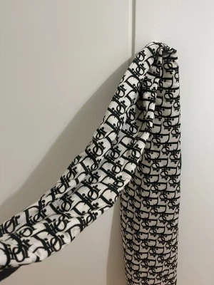 Christian Dior svartvit sjal - Snygg sjal från Christian Dior i svart och vitt med ikoniskt Dior-mönster och tydlig logga längs ena kanten. Tunt och mjukt material som känns lyxigt och passar perfekt till att lyfta din outfit. 